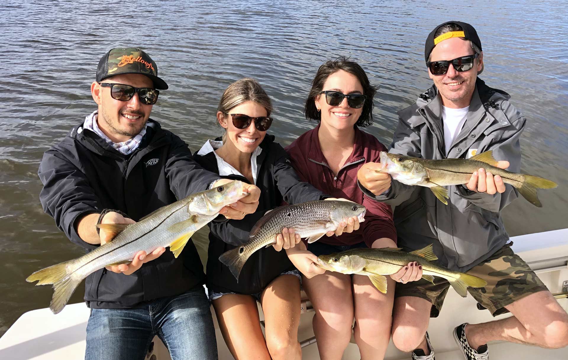 four people sitting on a boat and holding fish